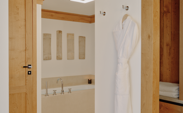 Accommodation suite at Aman Le Mélézin with wooden door, white towel and ensuite bathroom entrance.