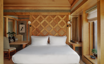 Suite bedroom at Aman Le Mélézin featuring a bed with geometric headboard and warm wooden finishes.