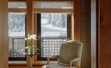 Wooden-framed reading nook at Aman Le Mélézin with upholstered chair overlooking snowy Alpine landscape.