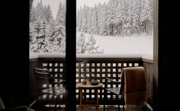 Snowy Alpine landscape viewed through suite windows at Aman Le Mélézin, with forest-lined slopes visible beyond.