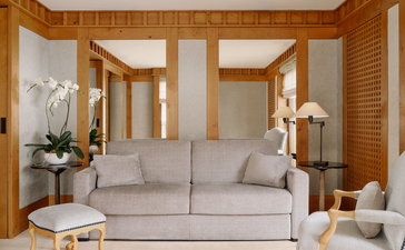 Suite lounge area at Aman Le Mélézin with cream sofa, wooden panelling and alpine views.