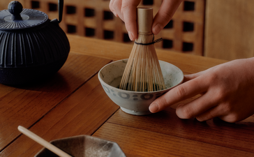 Hands preparing matcha tea at Aman Le Mélézin, whisking powder in a traditional bowl.