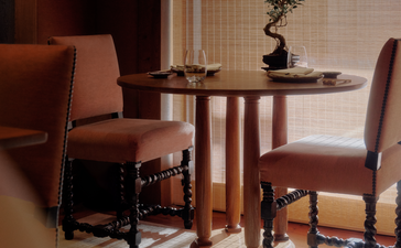 Dining area at Aman Le Mélézin with round wooden table, upholstered chairs, and geometric floor pattern.