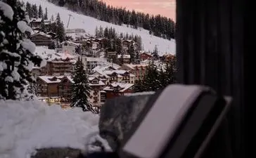 Sunlounger on a terrace at Aman Le Mélézin overlooking snow-covered Alpine slopes at dusk.
