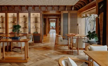 Spacious wooden interior at Aman Le Mélézin resort with natural light, featuring furniture and bathing area.
