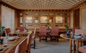 Warm dining room at Aman Le Mélézin with wooden furnishings, terracotta walls, and framed artwork.
