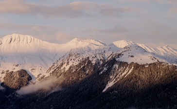 Snow-capped Alpine peaks rise above forested slopes and morning mist at Aman Le Mélézin, France.
