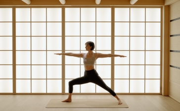 Personne en position de yoga guerrier devant les baies vitrées d'Aman Le Mélézin.