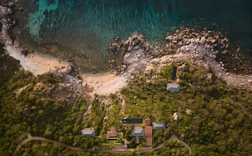 安缦诺怡度假村海滨别墅的空中俯瞰图，展示绿树环绕的建筑群与碧蓝海水相接。