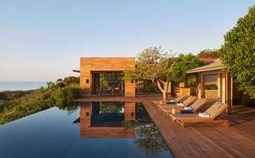 安缦诺怡度假村的海洋泳池别墅，木制餐饮亭台俯瞰宁静水面和远处山景。