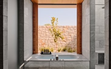 Bathroom window at Amanzoe resort framing views of golden Greek landscape and olive tree.