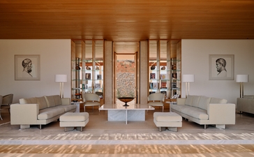 Sala d'ingresso con soffitti in legno, divani color crema e porte-finestre affacciate sul giardino, Amanzoe resort Grecia.