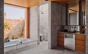 アマンゾイ リゾートの3ベッドルーム ヴィラのシャワールーム。石造りの壁、木製の洗面台、大きな窓から地中海の景色が見えます。