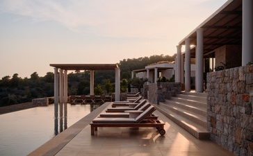 アマンゾイのリゾートにある3ベッドルームテラス。夕暮れ時、石造りの建物からテラスが広がり、インフィニティプールが望める。