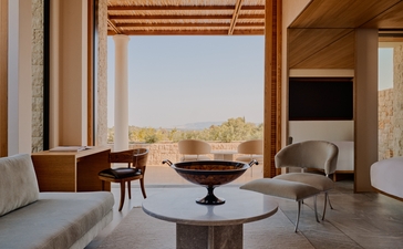 Villa with three bedrooms at Amanzoe resort, Greece, featuring open-plan living area with fireplace and views towards the landscape.