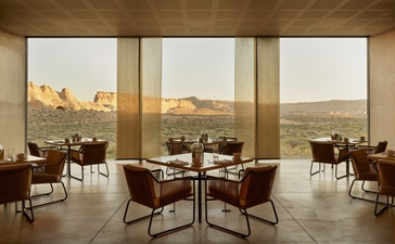Amangiri restaurant with floor-to-ceiling windows overlooking desert landscape, featuring round dining tables and mid-century modern seating.