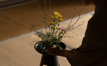 A hand arranging fresh flowers and branches in a dark vessel at Aman Kyoto.