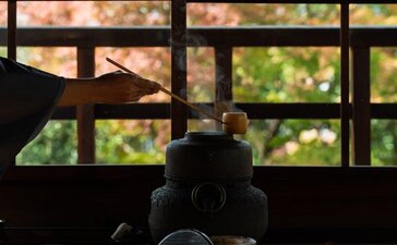 Silhouetted tea ceremony utensils arranged on a low table at Aman Kyoto, with garden views beyond latticed windows.
