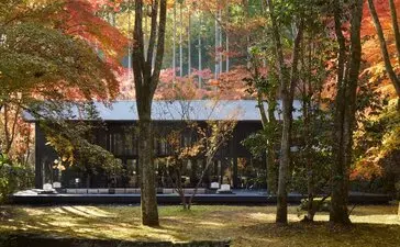 Pavilion exterior at Aman Kyoto resort surrounded by autumn foliage and tall trees.