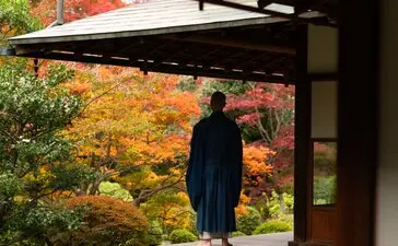 Visitor admiring autumn foliage from a covered pavilion at Aman Kyoto resort.