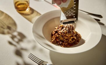 Plated dish at Aman Venice dining venue, with chef pouring golden sauce over a composed food arrangement.