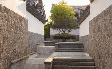 Stone pathway with steps leading to a courtyard at Amandayan, China, framed by modern architectural walls.