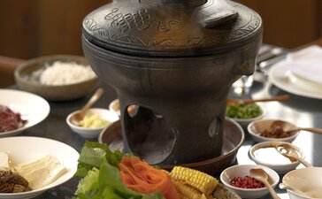 Nixi black pottery hot pot with steam rising, surrounded by small bowls and fresh ingredients at Amandayan.