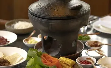 Nixi black pottery hot pot with steam rising, surrounded by small bowls and fresh ingredients at Amandayan.
