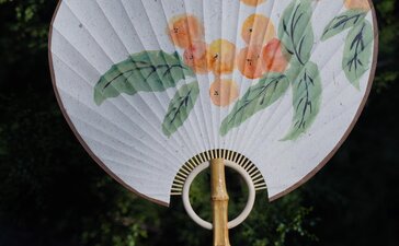 Traditional Chinese fan with painted orange flowers and green leaves, displayed at Amandayan.