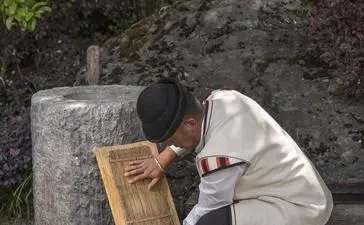 Artisan demonstrates traditional Dongba paper-making technique at Amandayan, working with handmade paper frame outdoors.
