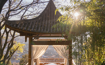 Sunrise light filters through trees beside a traditional pavilion at Amandayan, China resort.