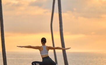 アマンプリ リゾートで、夕焼けを背景に海辺でヨガのポーズを取る人物。