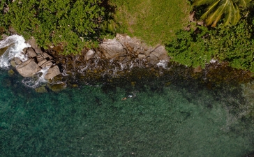 Luftaufnahme der Küste von Amanpuri Resort an der Andamanensee mit türkisfarbenem Wasser und felsigen Ufern.