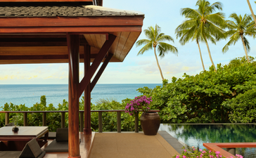 アマンプリのパビリオン宿泊施設の屋外エリア。木製の屋根付きテラスから、ヤシの木越しにタイの海が見える。