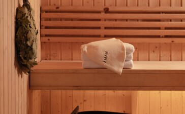 アマンプリのスパ施設内にある木製サウナ小屋。木製のベンチに白いタオルと瓶が置かれ、床には黒い桶とひしゃくがある。