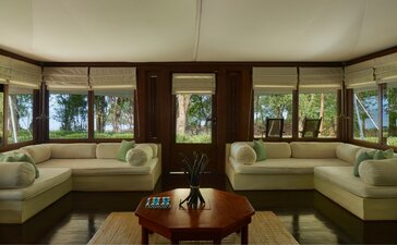 Amanwana jungle tent living area with curved seating arrangement and floor-to-ceiling windows overlooking tropical forest.