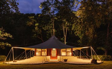 Amanwana jungle tent illuminated at dusk, surrounded by Indonesian rainforest.