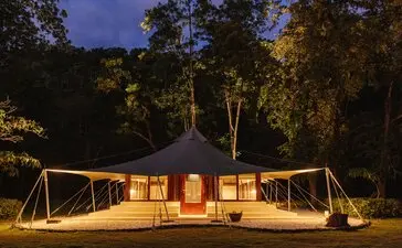 Amanwana jungle tent illuminated at dusk, surrounded by Indonesian rainforest.