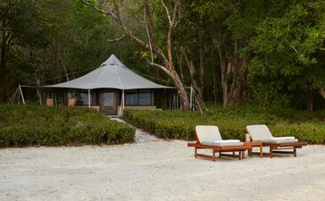 Ocean front tent at Amanwana with lounge chairs on sandy beach, Indonesia.