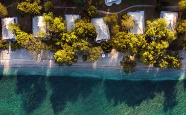 Aerial view of oceanfront tent accommodation at Amanwana, Indonesia, with turquoise waters below.