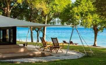 Ocean-front tent at Amanwana with loungers on the lawn overlooking the sea, Indonesia.