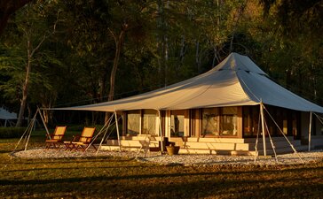 Canvas tent illuminated at dusk at Amanwana, Indonesia, with ocean view and surrounding trees.