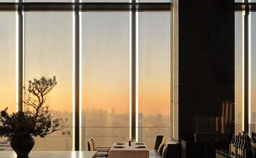 Arva interior at Aman Tokyo with floor-to-ceiling windows overlooking sunset over the city.