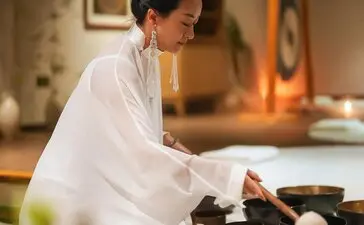 Woman in white shirt preparing tea at Amanfayun, with traditional pottery and candles on table.