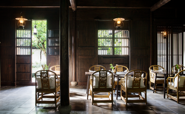 Amanfayun steam house dining room with dark timber columns, wooden chairs, and windows overlooking gardens.