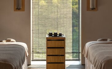 Spa treatment room at Amanyangyun with two massage beds facing a large window and central wooden cabinet.