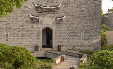 Stone pavilion at Amanyangyun with traditional curved roof and timber pathway through manicured garden.