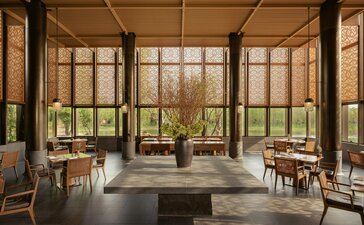 Sunlit interior at Amanyangyun with floor-to-ceiling windows framing garden views, wooden furniture, and potted plants.