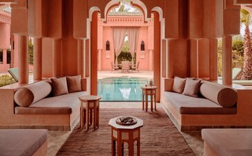 安缦珍纳度假村的两卧室泳池别墅，红土色建筑内设室内泳池、起居区及对称布局的座位。