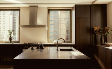 Modern kitchen at Aman New York with dark cabinetry, white marble countertop, and stainless steel appliances.